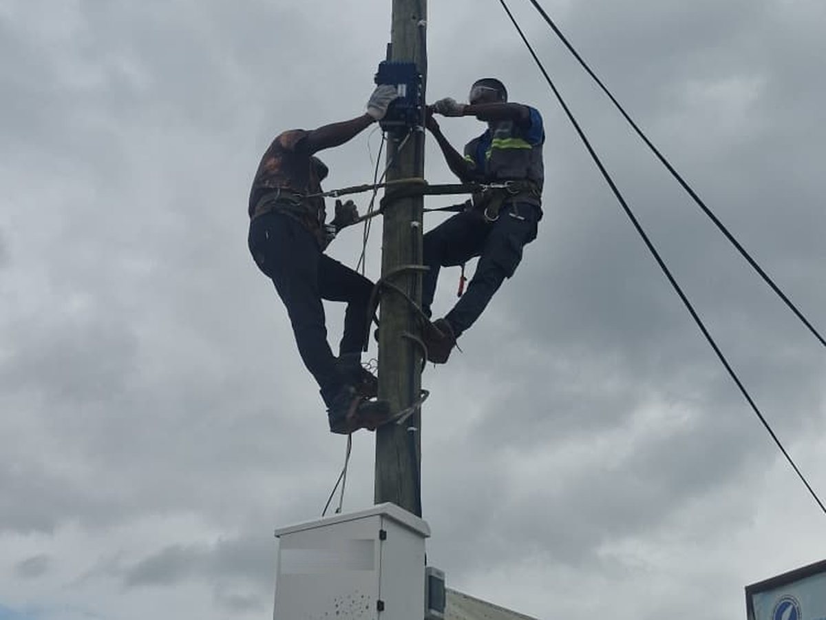 Two Multicom linesmen working at height on a distribution pole, over the cabinet they are feeding