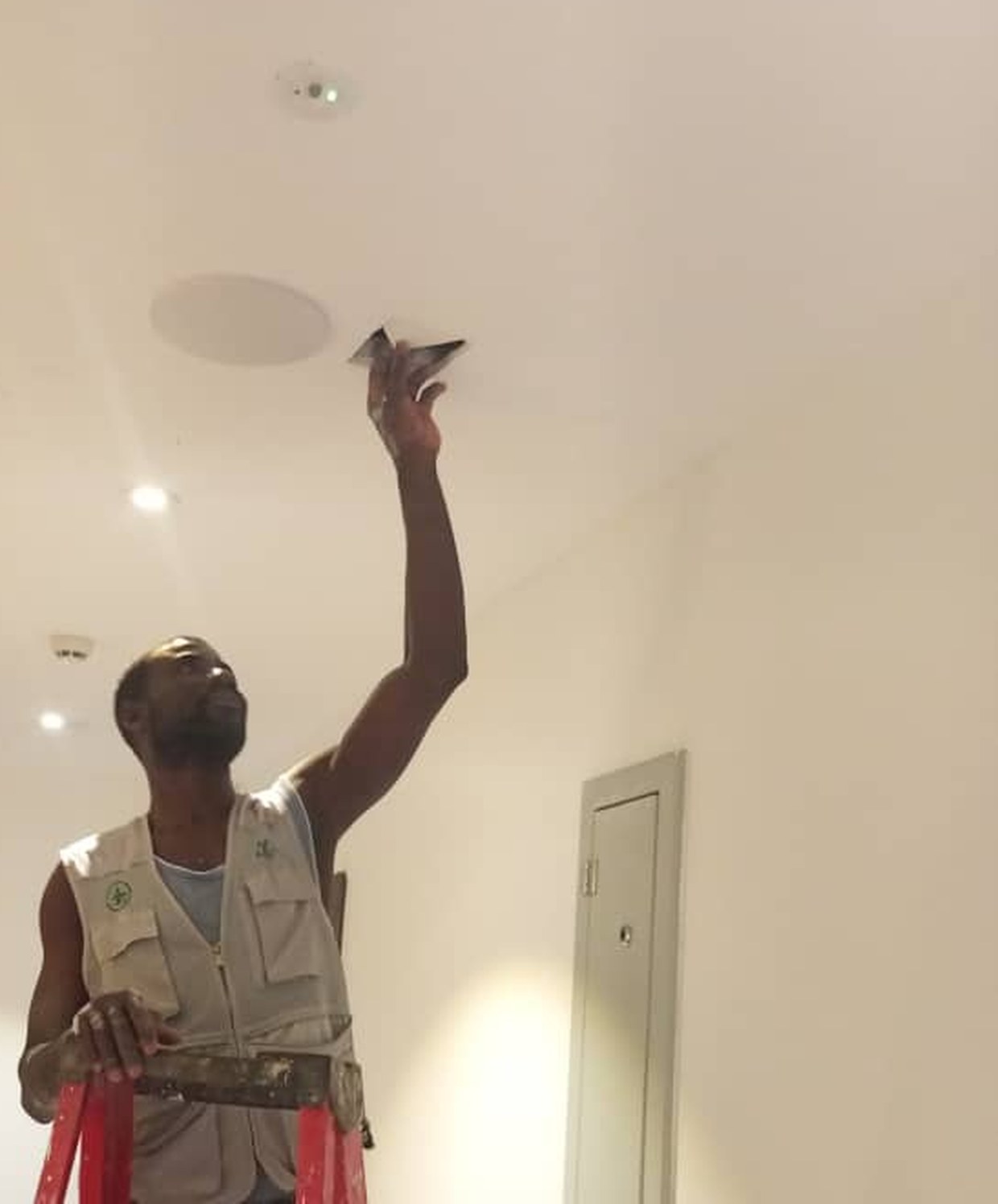 A Multicom technician fitting a ceiling antenna into a corridor slab, beside the service riser it is fed from
