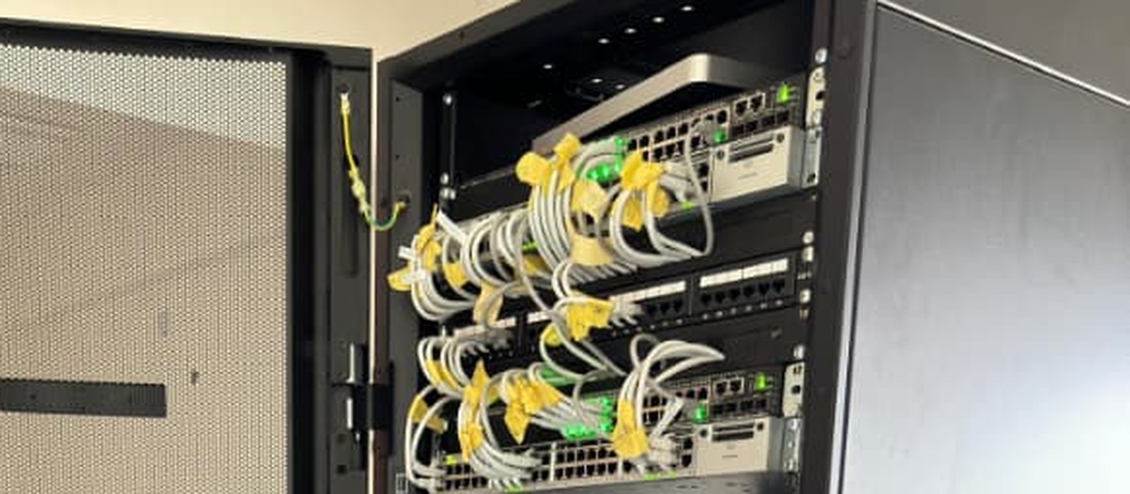 Fibre and copper patch leads landed on panels and run into managed switches inside an open floor-standing rack, link lights lit