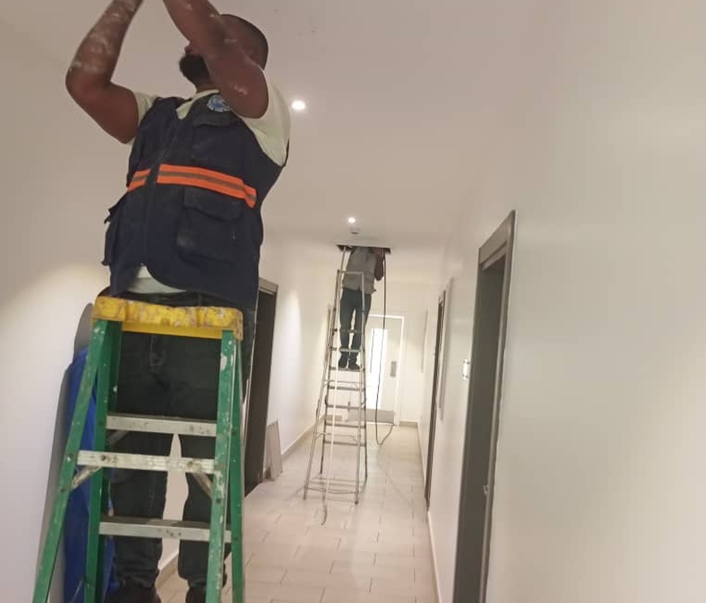 Two Multicom technicians on ladders in a corridor, working into an open ceiling void, with a third further down the hall